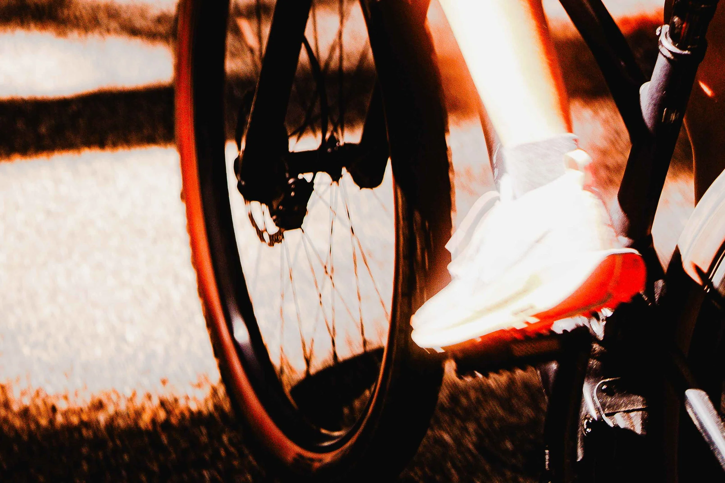 Une vue en plongée d'un vélo avec son pneu avant, à côté d'une chaussée en béton et une personne portant une chaussure de sport.