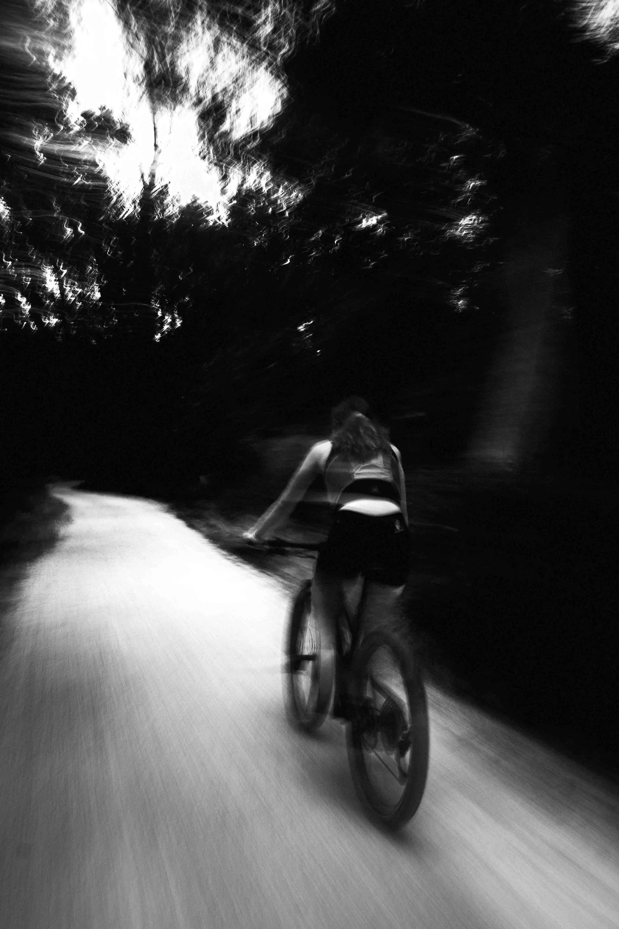 Une personne à vélo roulant dans une rue sombre la nuit, avec un ciel étoilé ou éclairé en noir et blanc.