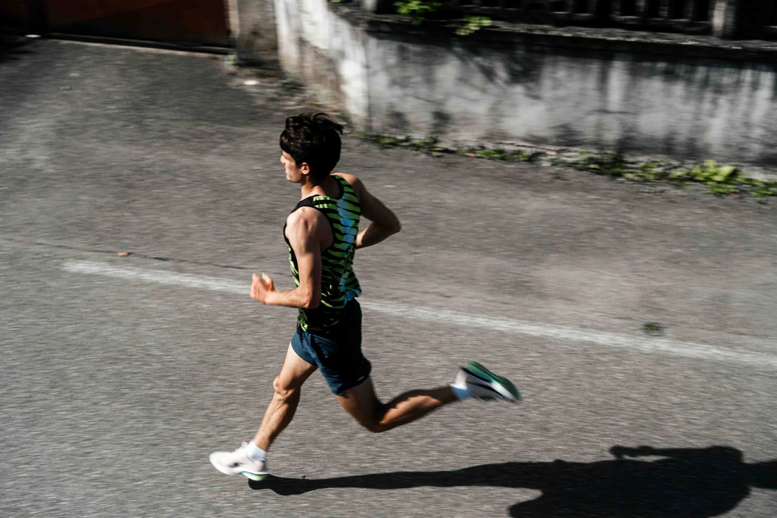 Un homme court sur une route en portant une tenue de sport à rayures vertes et noires.