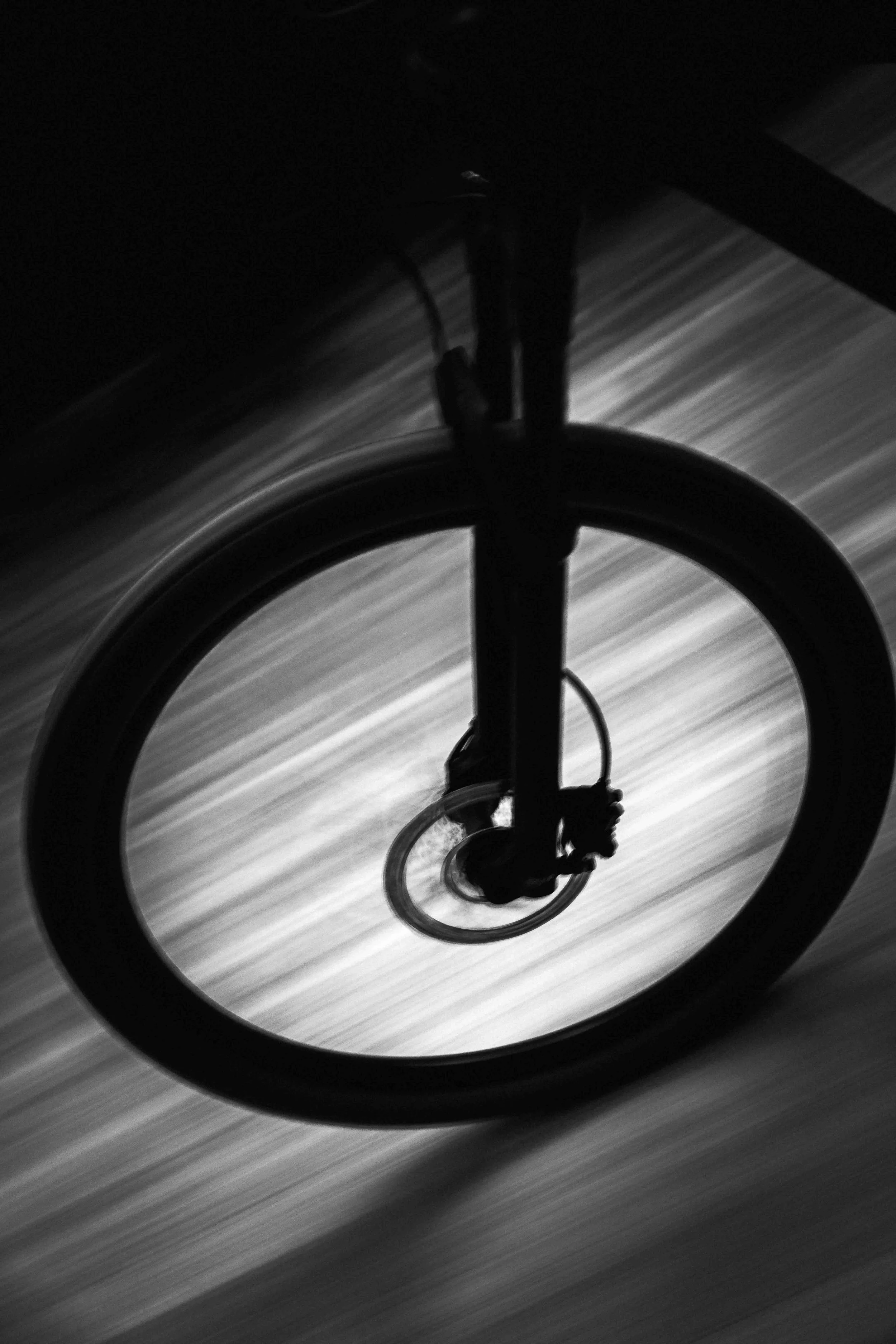 Photo en noir et blanc de la vue d'une roue de vélo en rotation vue de dessous, avec un arrière-plan flou.