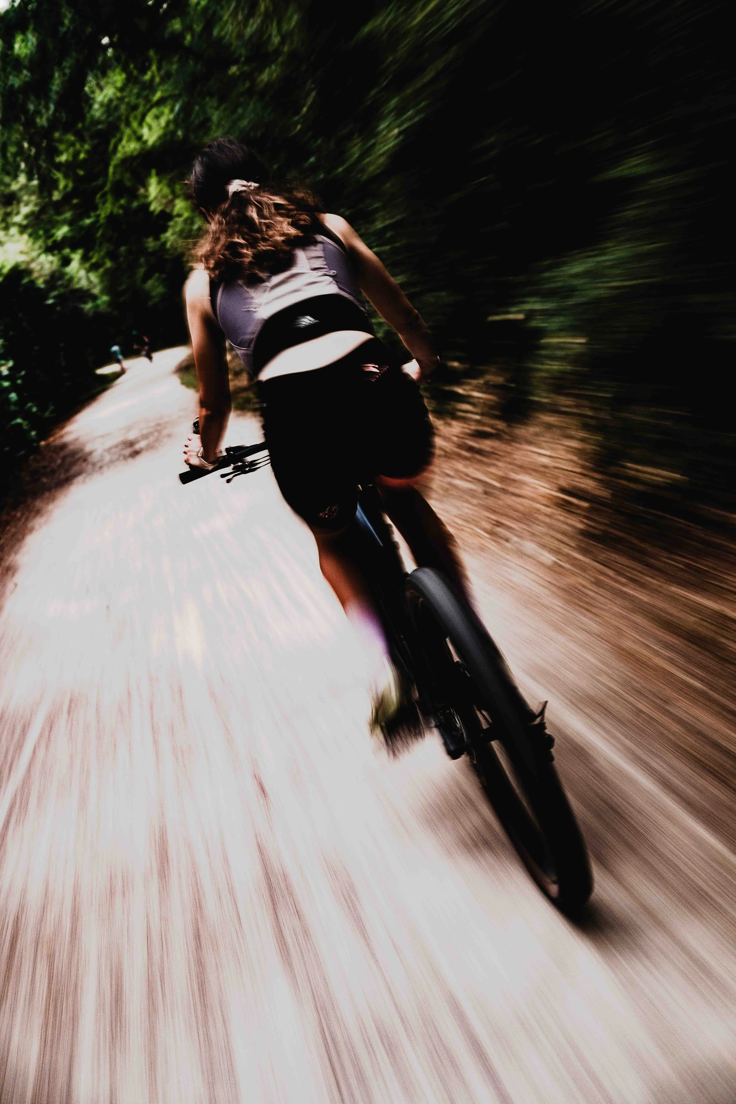 Une jeune femme fait du vélo sur un chemin dans une forêt, vue de derrière, avec un effet de vitesse et de mouvement.