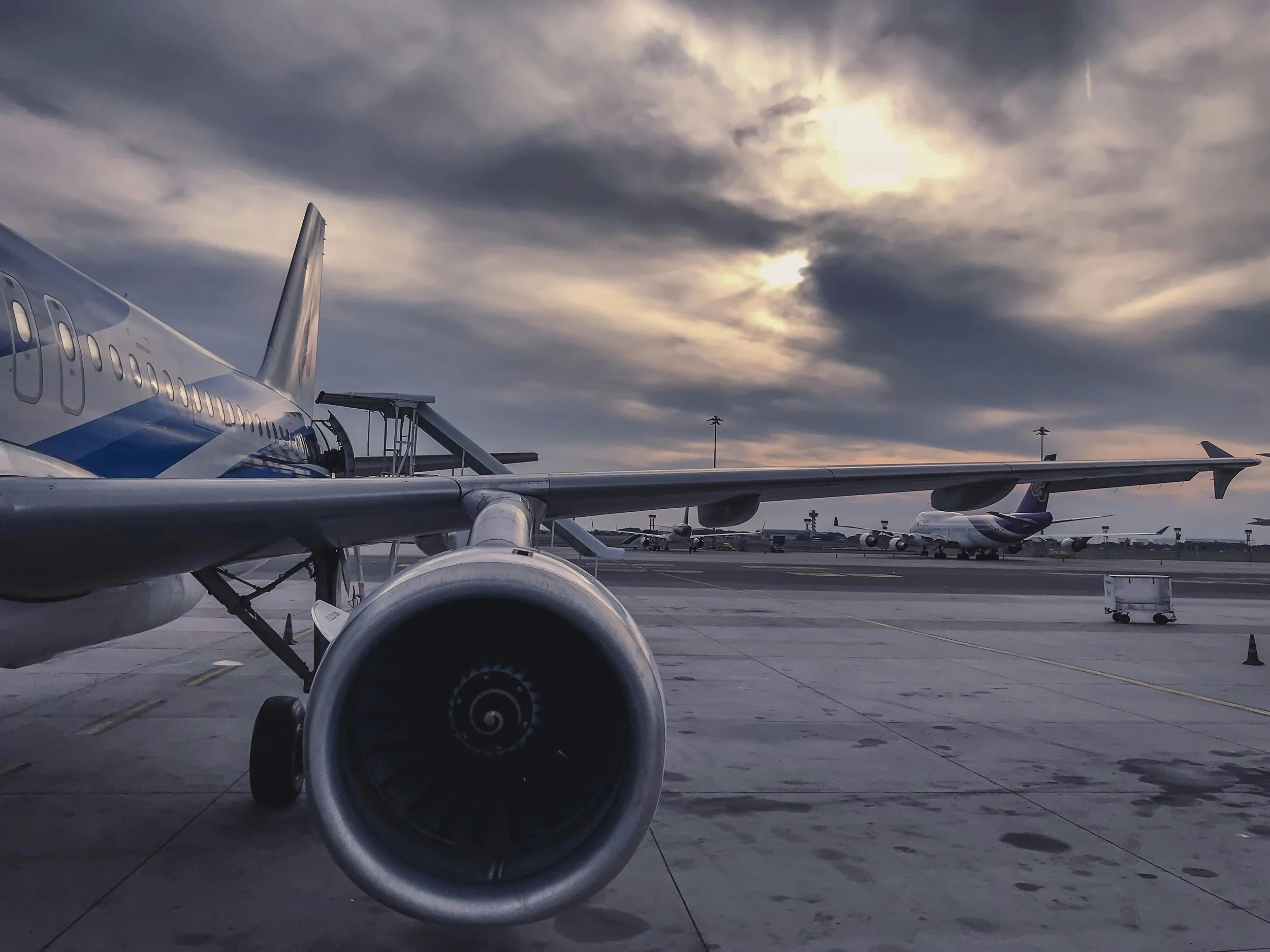 View of airplanes parked on an airport tarmac under a cloudy sky at sunset.