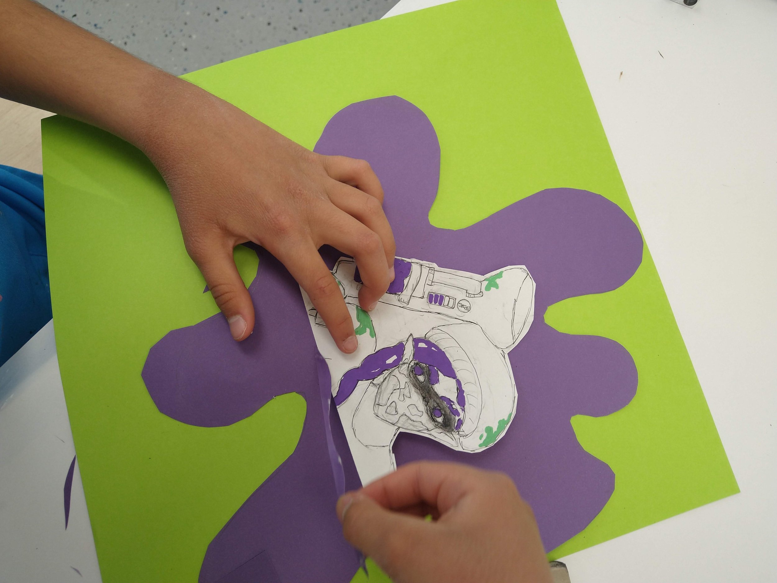 Child creating a butterfly collage on a green background using purple paper and a black-and-white printed image of a robot.
