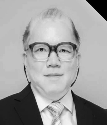 Black and white photo of a man wearing glasses, a suit, and a tie.