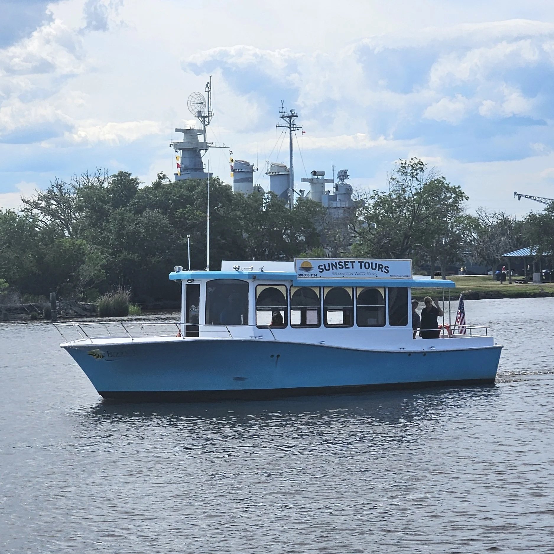 A white boat named Sunset Tours on a river with trees and clouds in the background.