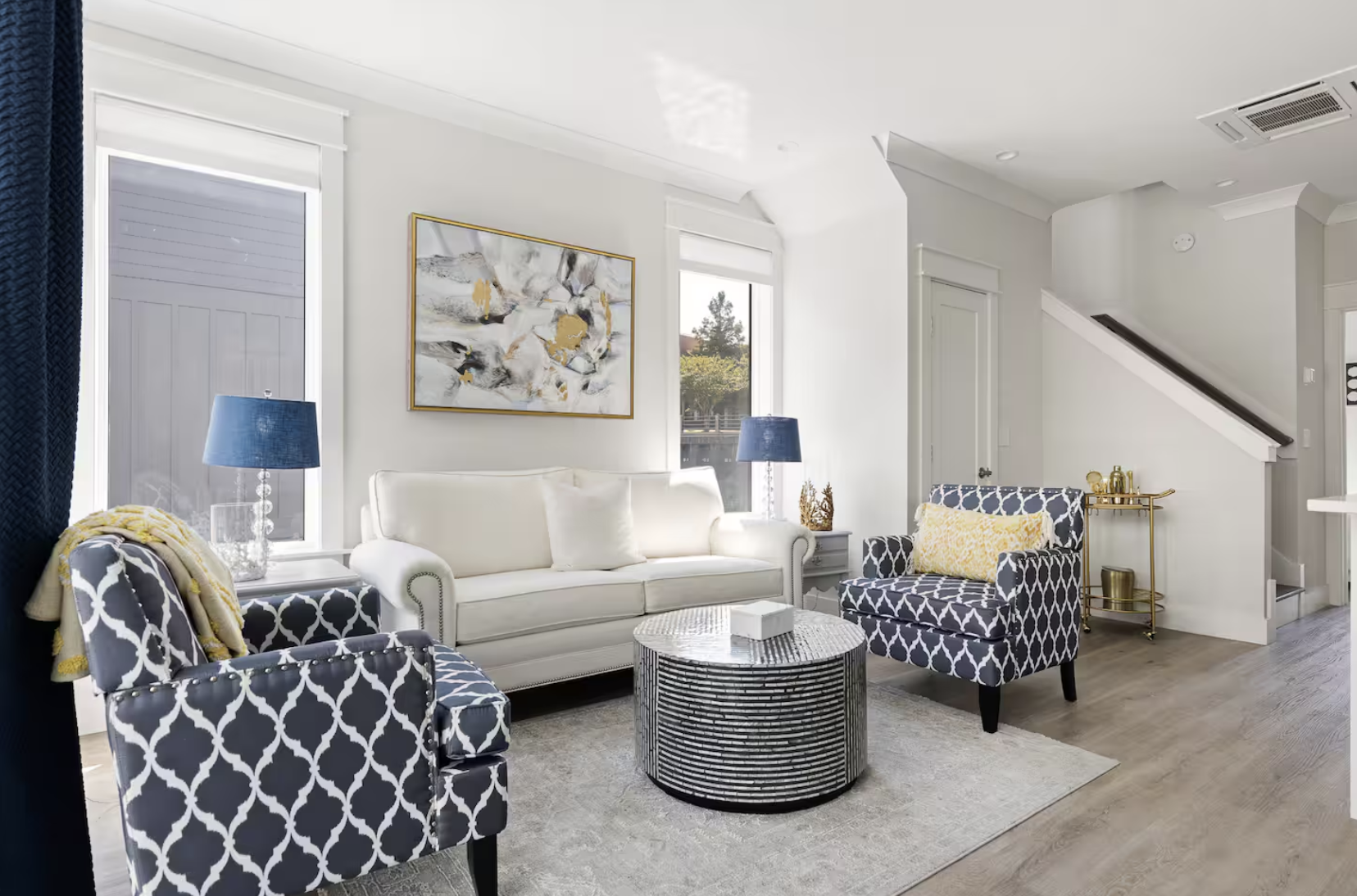 Modern living room with white sofa, two patterned armchairs, abstract wall art, two blue lamps, and gold accents