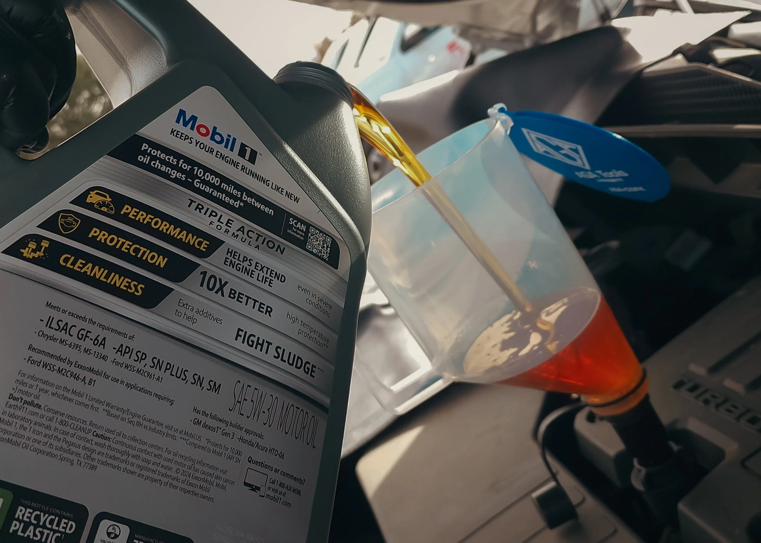 Pouring engine oil from a Mobil 1 bottle into a translucent container for measuring.