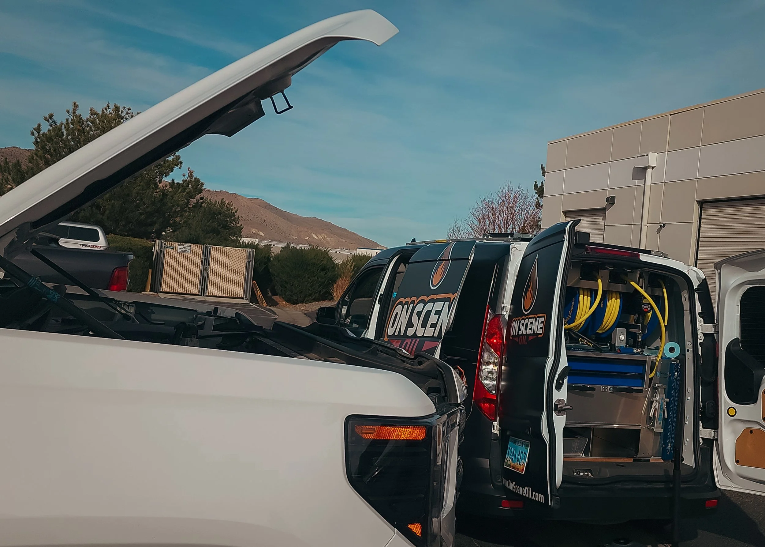 A work truck with ON SCENE Oil branding parked outdoors near a building, with its side door open revealing yellow hoses and equipment inside.