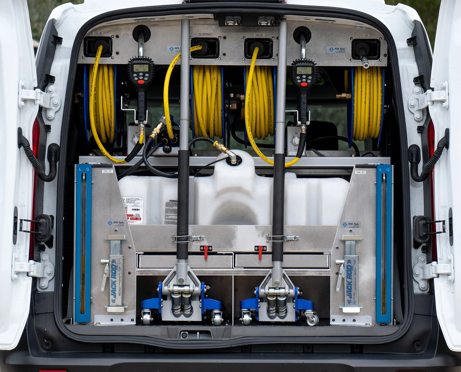 The back compartment of a utility van equipped with cleaning or maintenance equipment, including yellow hoses, meters used for mobile oil change service..