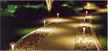 A landscaped pathway illuminated by small ground lights along both sides at night.