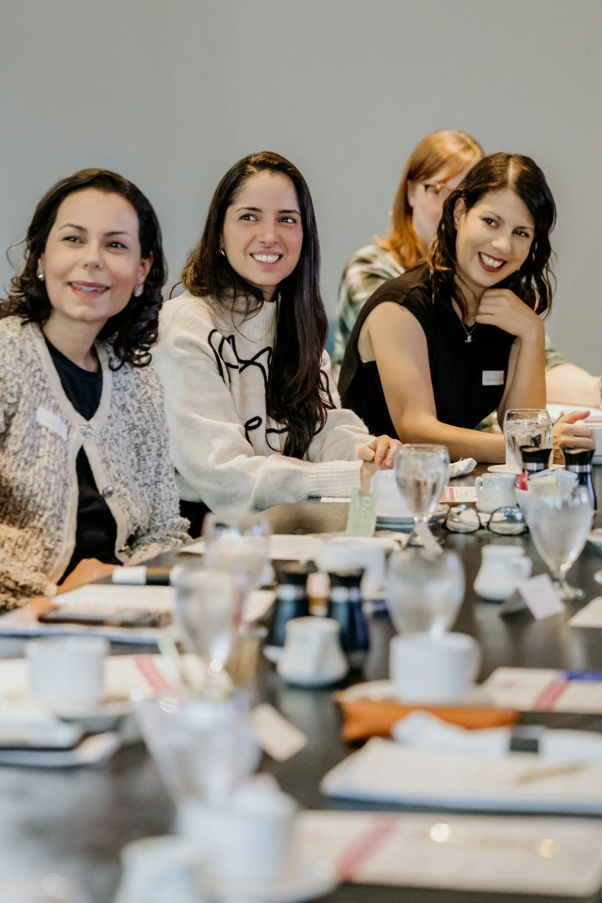 Group of women sitting at a table during a meeting or conference, smiling and engaging.