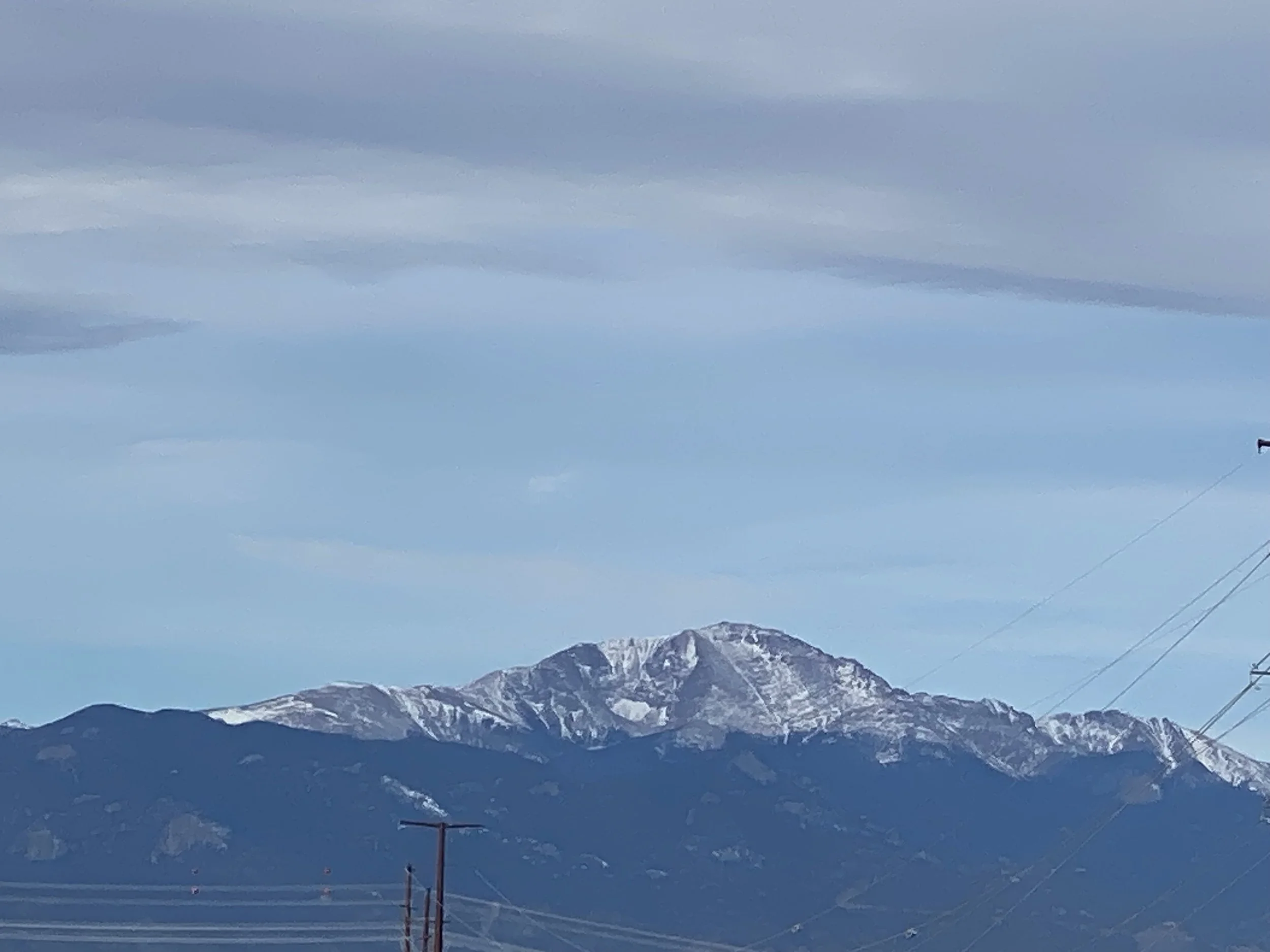 Snow-capped mountain range under cloudy sky, with power lines in foreground.