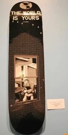 Skateboard deck painted with a scene from the original Scarface film, a gangster with a gun looking out a window that has been shot up, above the worlds "The World is Yours" with a globe