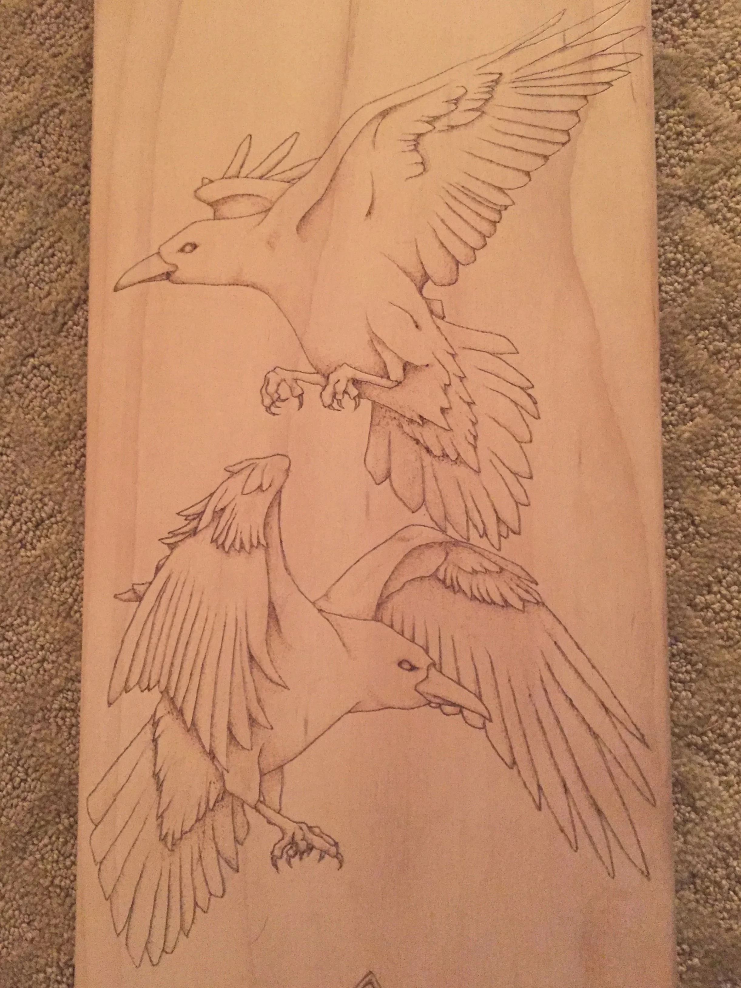 A wood skateboard deck with two ravens wood-burned into the surface