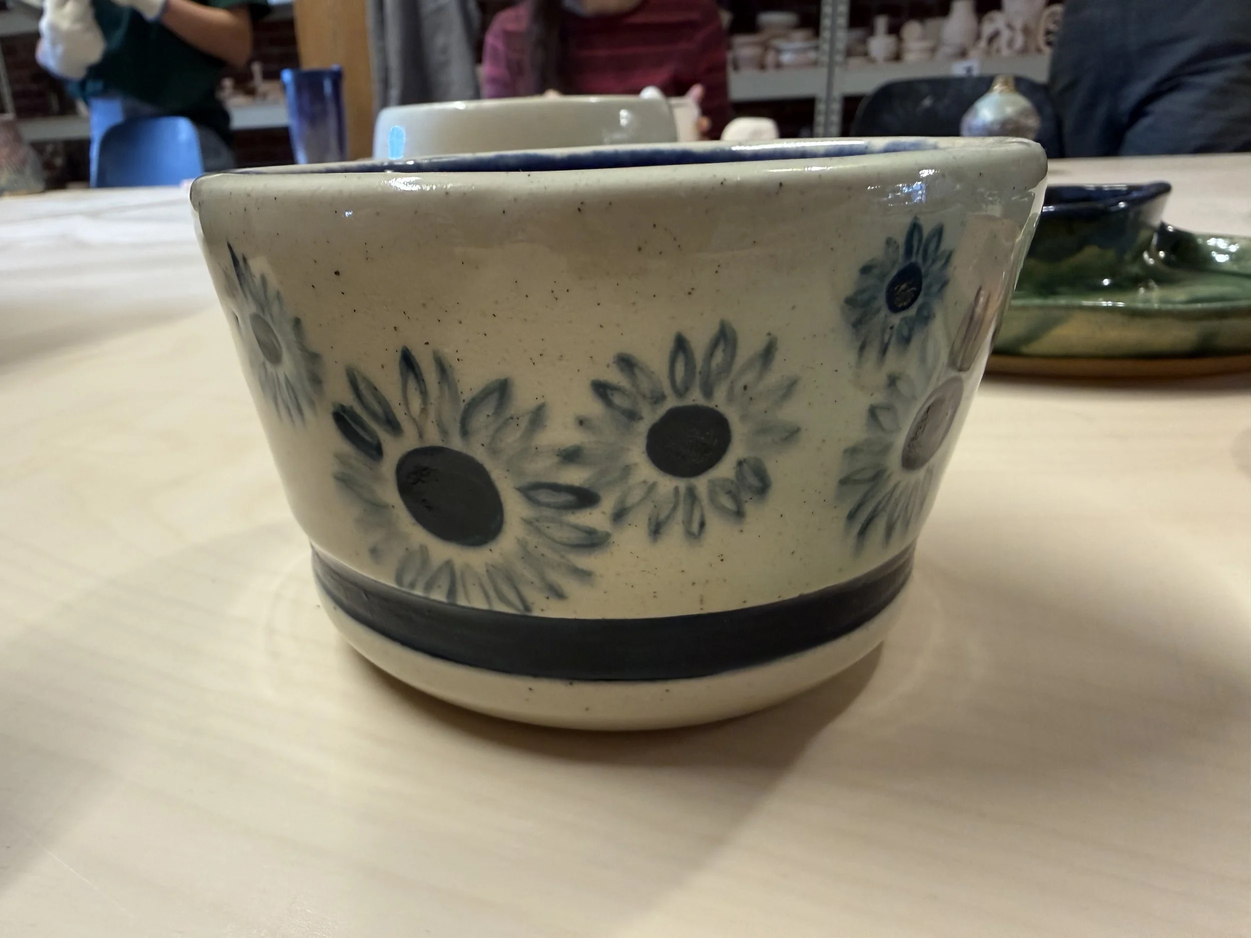 Small white plant pot decorated with blue daisies and a blue band toward the bottom.