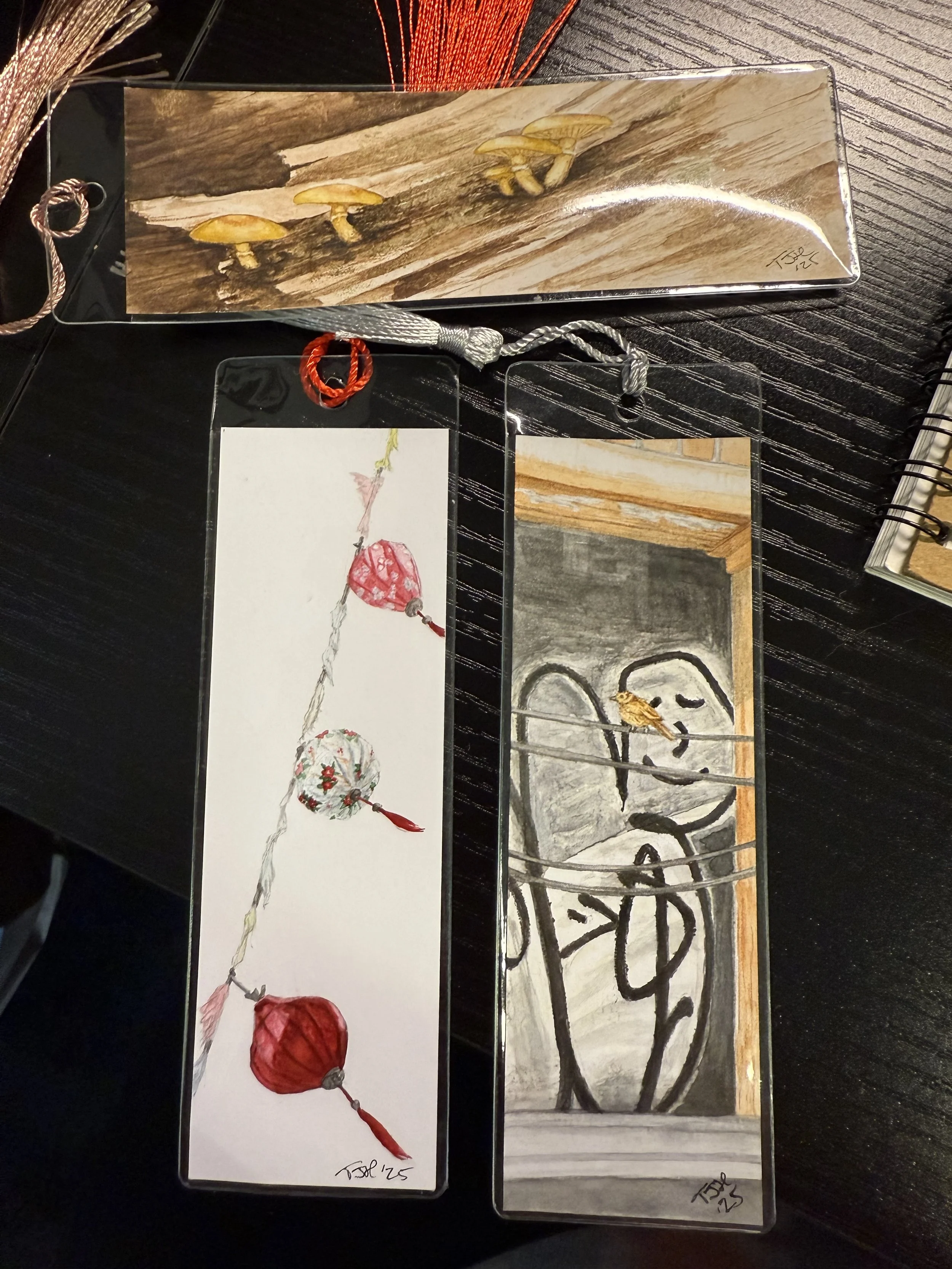 Three hand-painted bookmarks, one with mushrooms in a tree, one with Chinese lanterns, and one with a bird in front of graffiti.