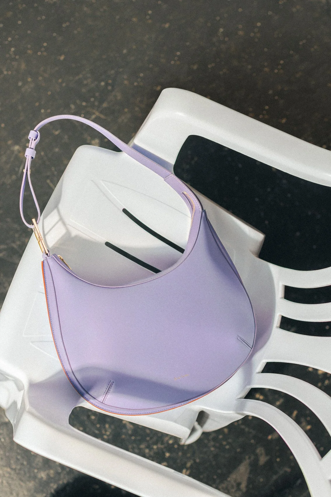 A purple handbag resting on a white plastic chair outdoors.