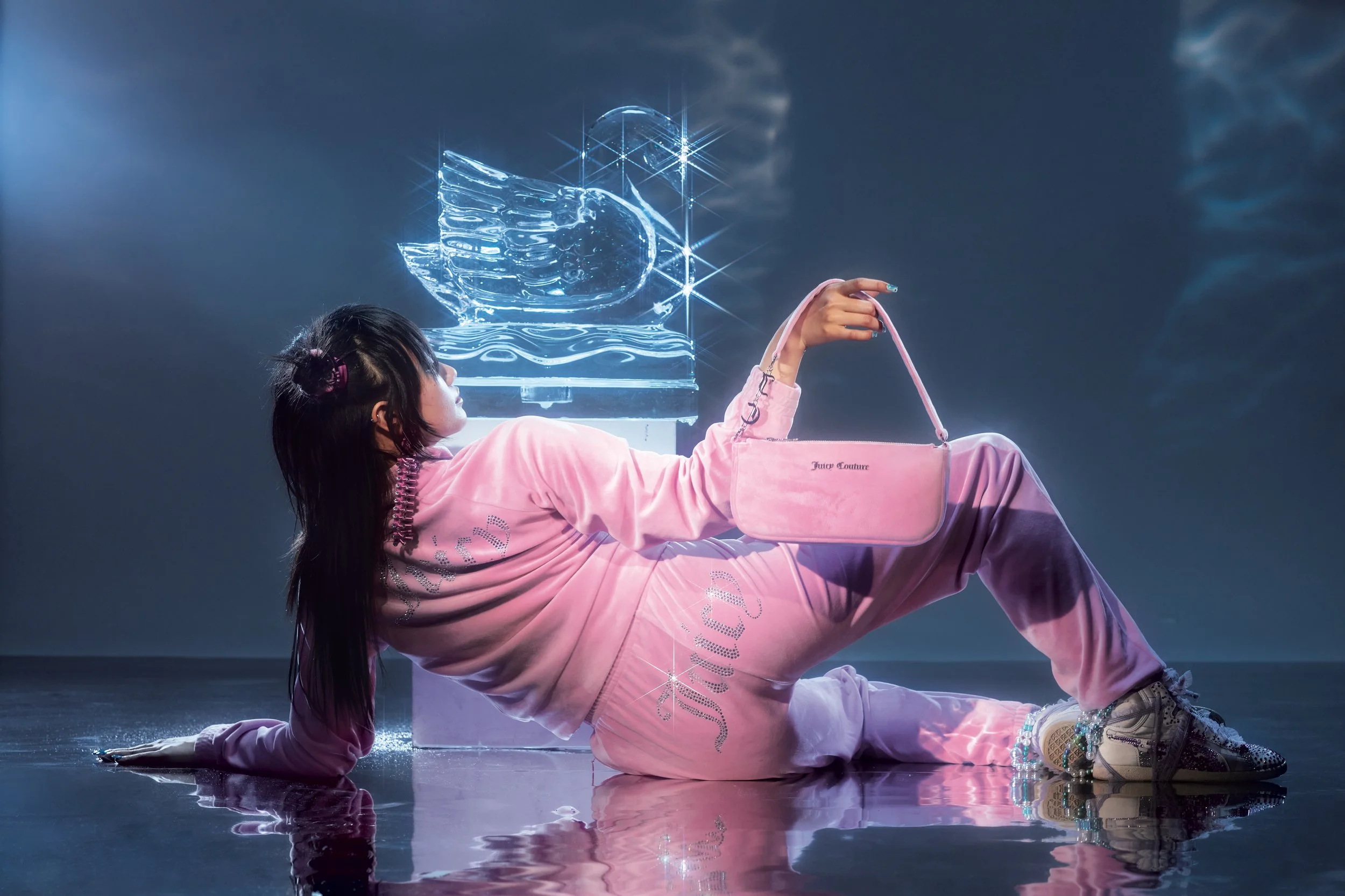 A woman in pink clothing lying on a reflective surface, holding a pink purse, with a glowing, digital-looking abstract shape in the background.