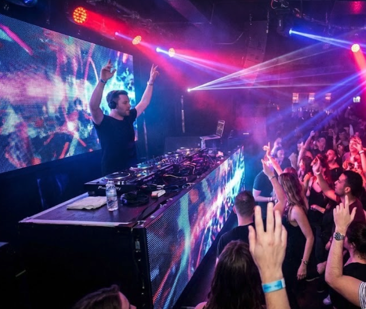 DJ performing at a nightclub with colorful laser lights and a cheering crowd.