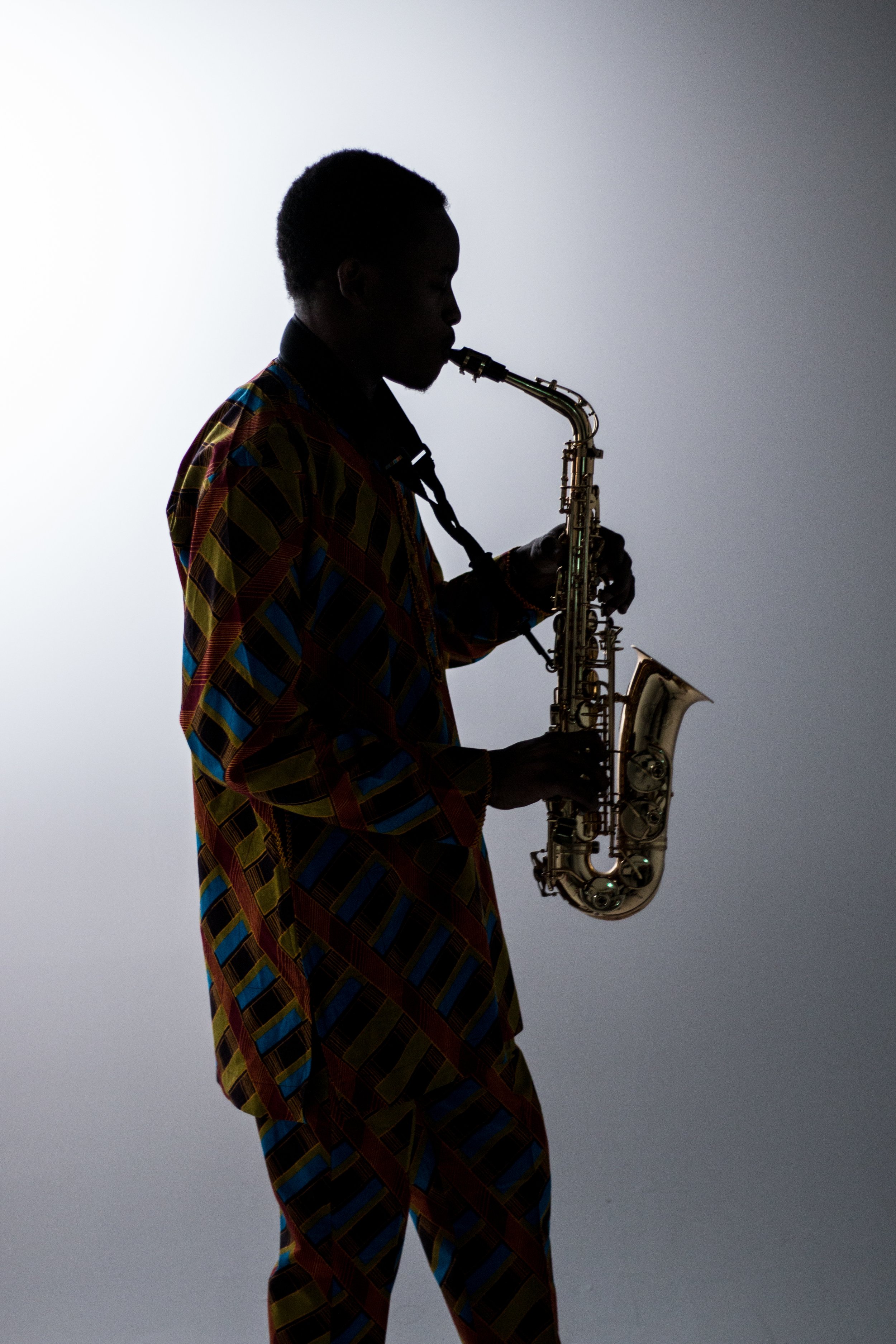Silhouette of a person playing a saxophone against a plain, light background.