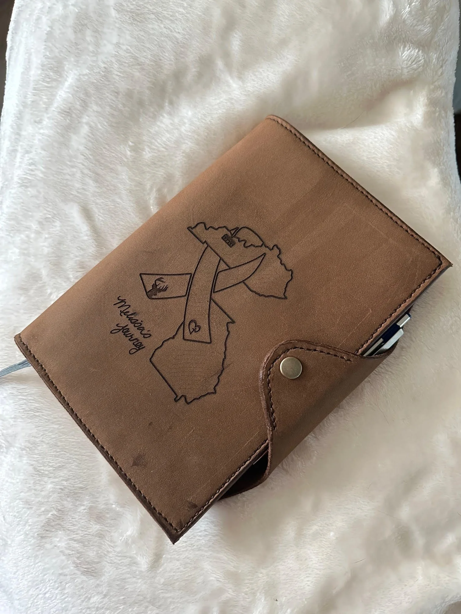 A brown leather planner with a map of the Philippines and a heart drawn on it, with the words 'Mahal ko you' written inside a message bubble, resting on a white fuzzy surface.