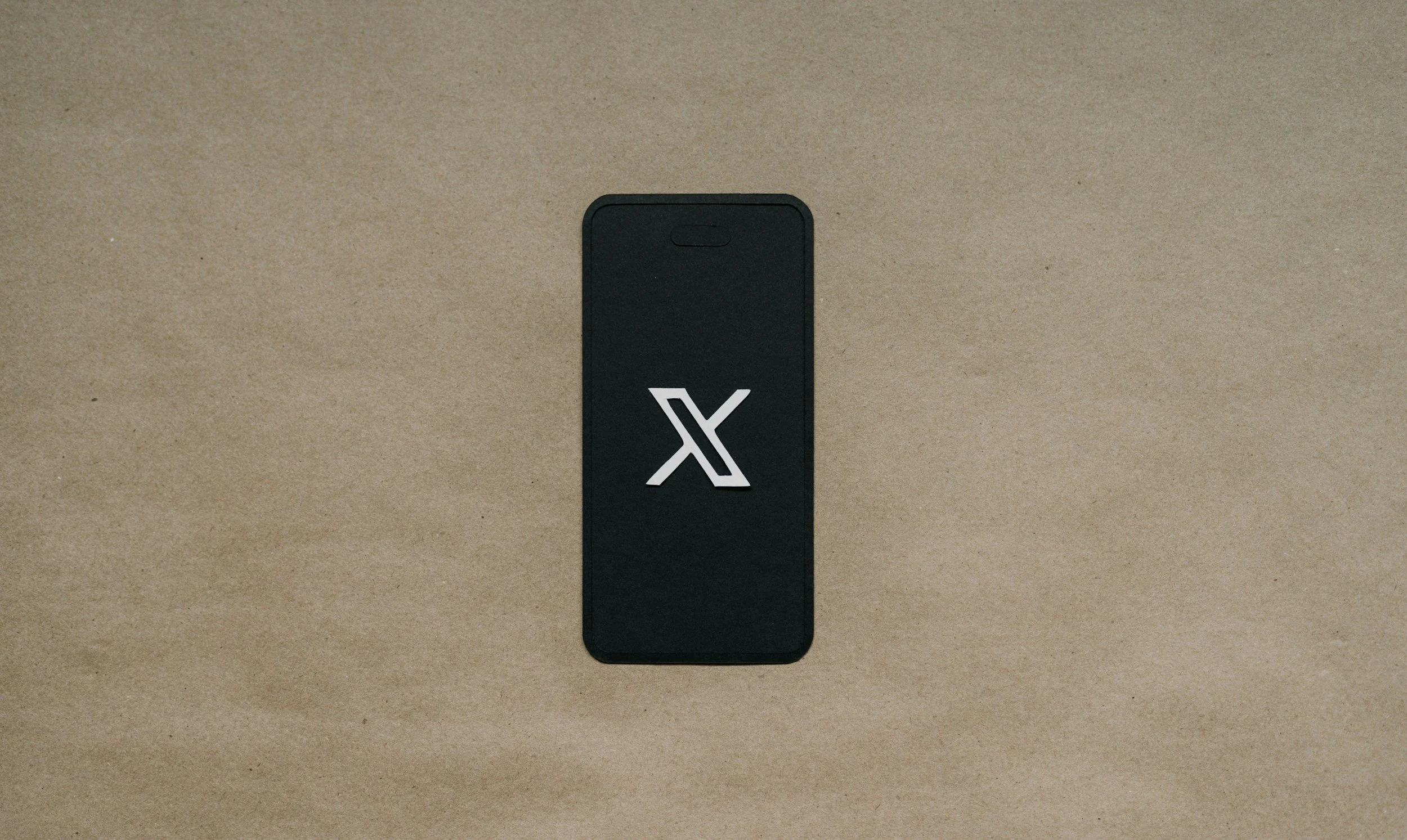 Black smartphone lying on brown surface with a logo in the center of the screen.