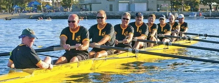A team of eight rowers in a yellow boat with their coach on a body of water.