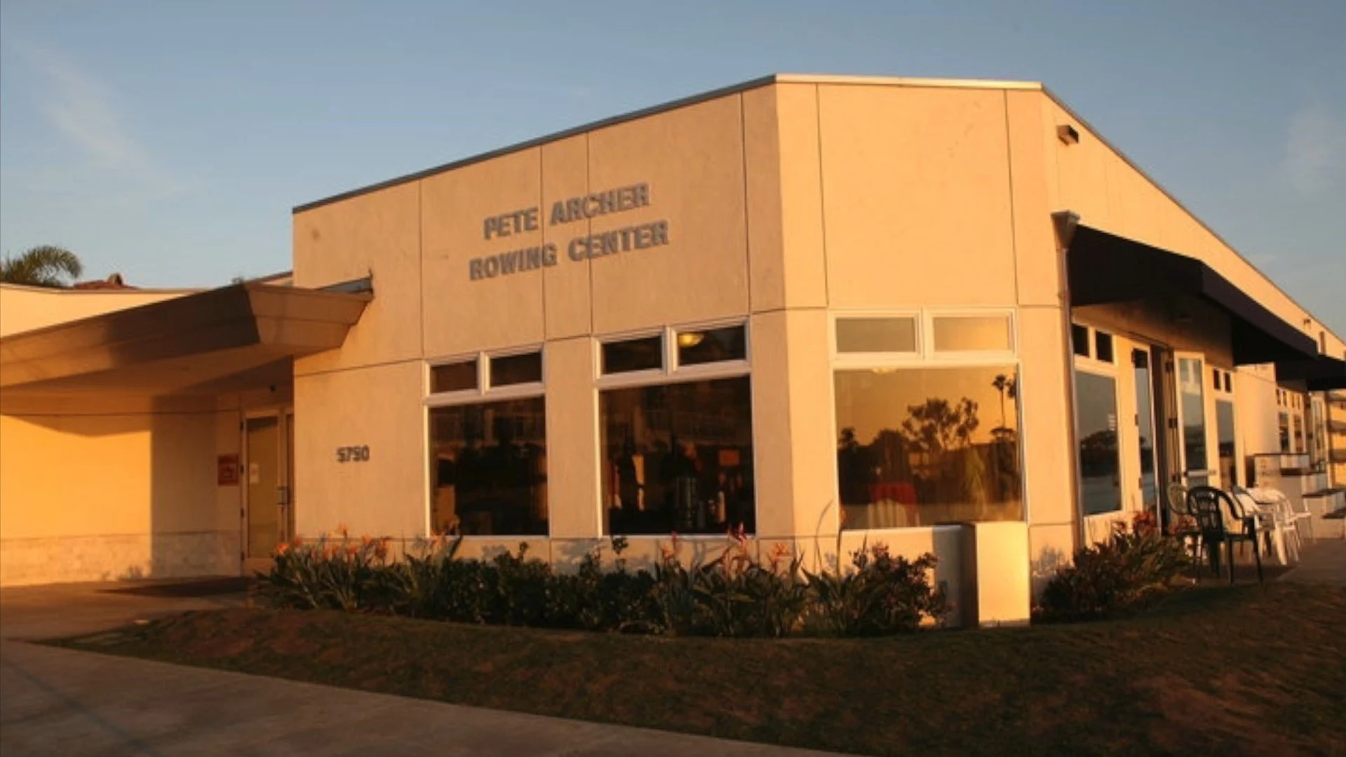 Exterior of the Pete Archer Rowing Center building during sunset with large windows and outdoor seating.