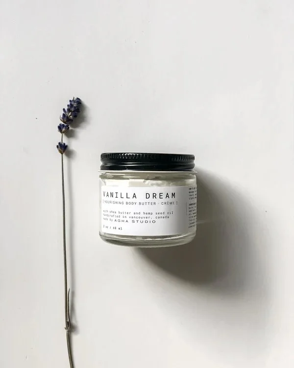Jar of Vanilla Dream nourishing body butter on a white surface with a lavender flower