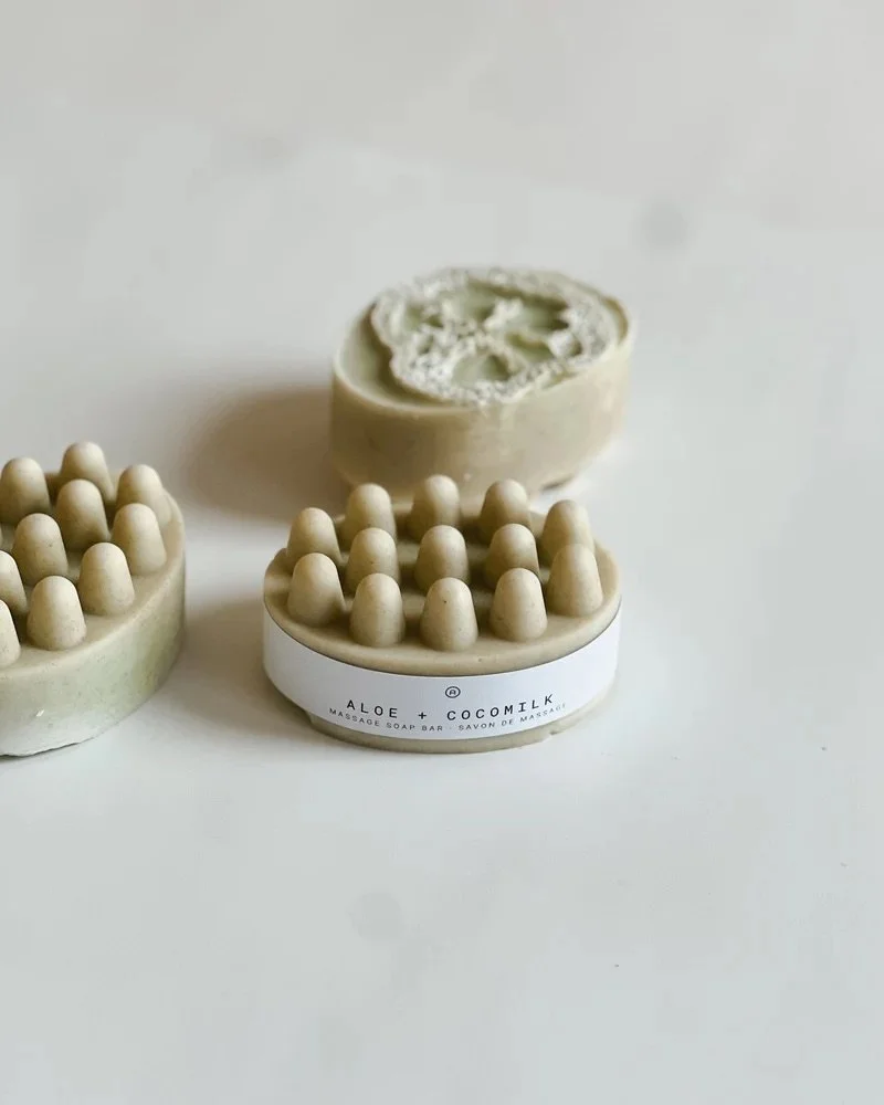 A massage soap bar with a white label reading 'Aloe + Cocomilk' and two other soap bars with massage nodes on a white surface.