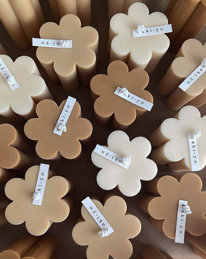 Assorted beige and cream-colored candles shaped like flowers, each with a small paper label attached that says 'caki.yo'.