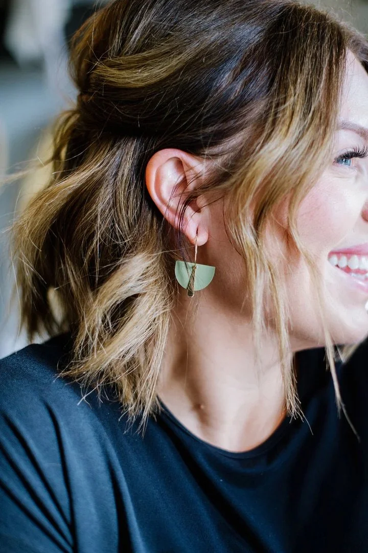 Close-up of a woman with shoulder-length, wavy brown hair with blonde highlights, wearing a unique geometric-shaped earring.