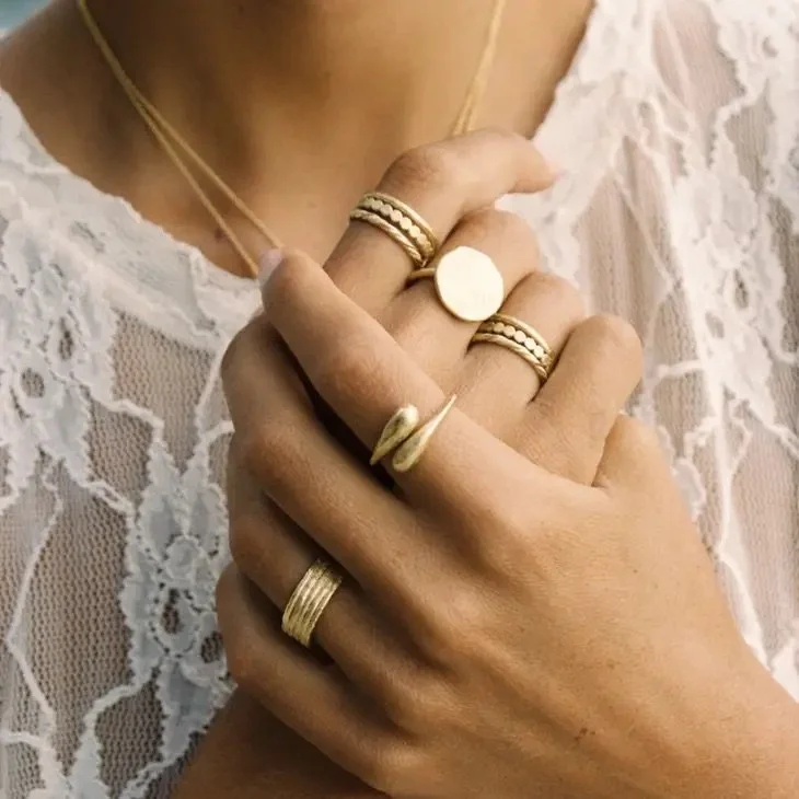 Close-up of multiple gold rings on fingers and a necklace on a woman wearing a white lace top.