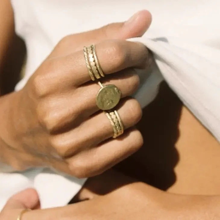 A hand adorned with gold rings holding a coin, with a white fabric background.