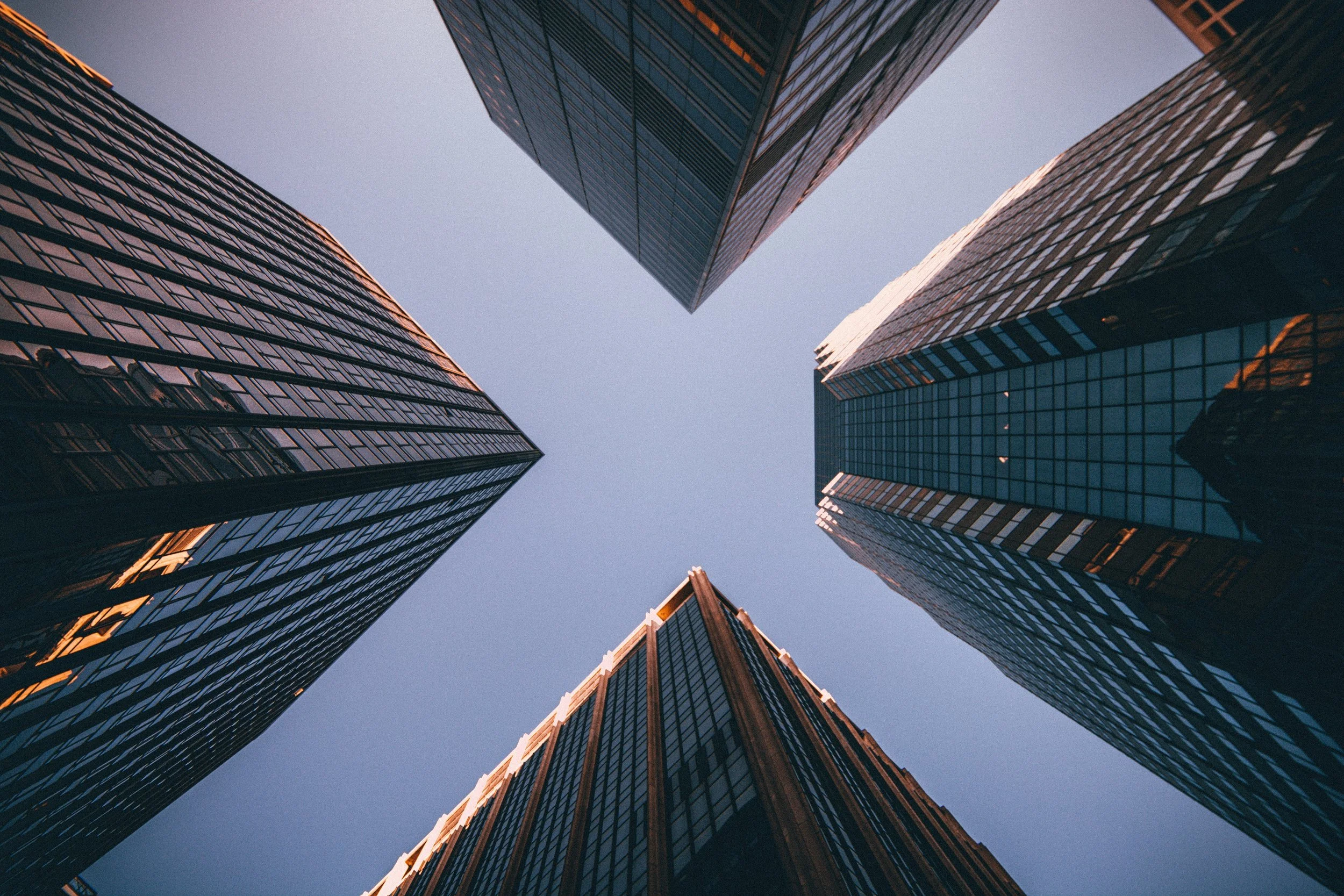 Looking up at tall modern glass skyscrapers in a city, capturing the buildings from a low angle against a clear sky.