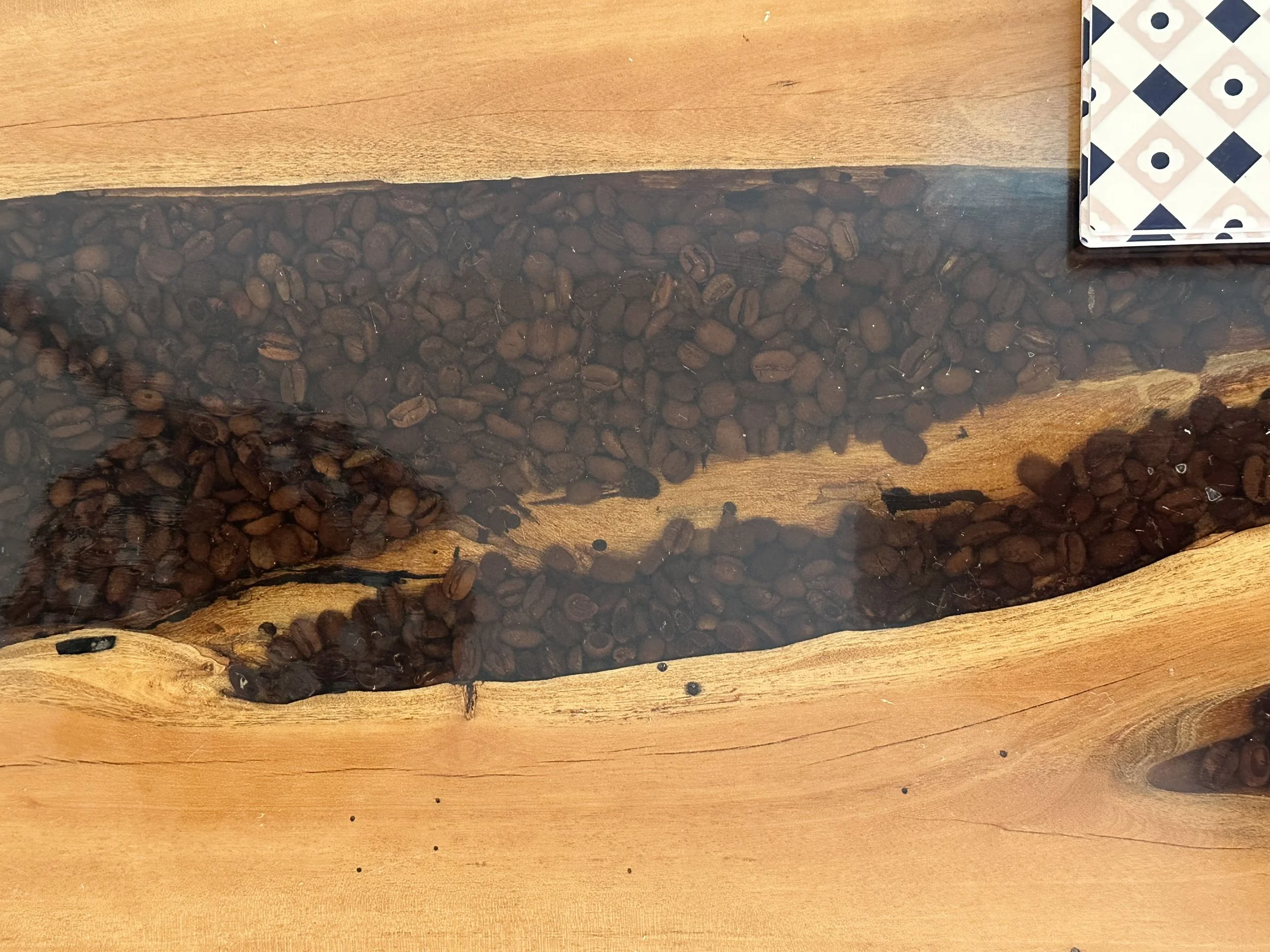 Close-up of a wooden table with a resin inlay filled with coffee beans and a partially visible deck of playing cards in the top right corner.
