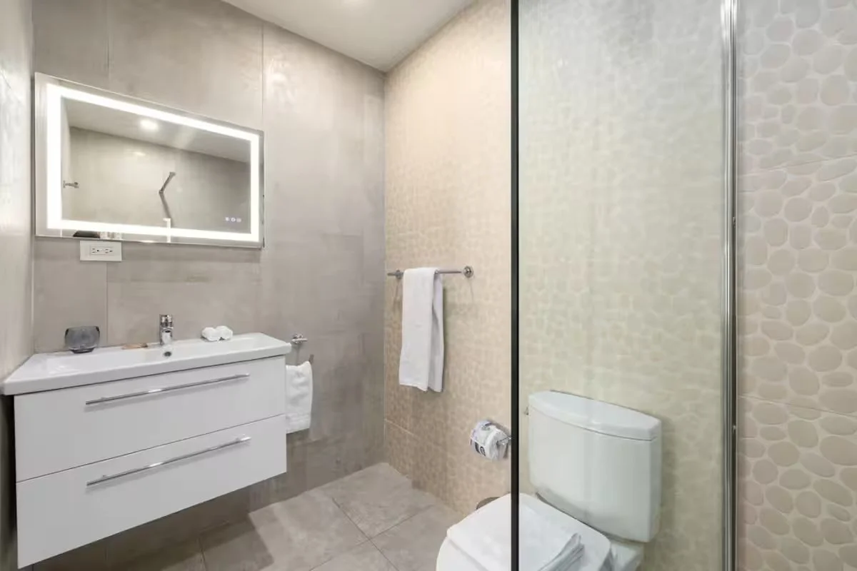 Modern bathroom with a white vanity, illuminated mirror, toilet, and tiled walls and floor