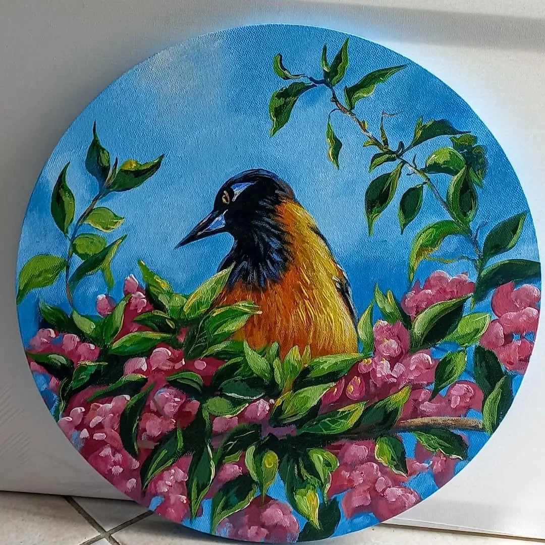 A circular painting of a bird with black and orange feathers sitting among pink flowers and green leaves against a blue sky background.