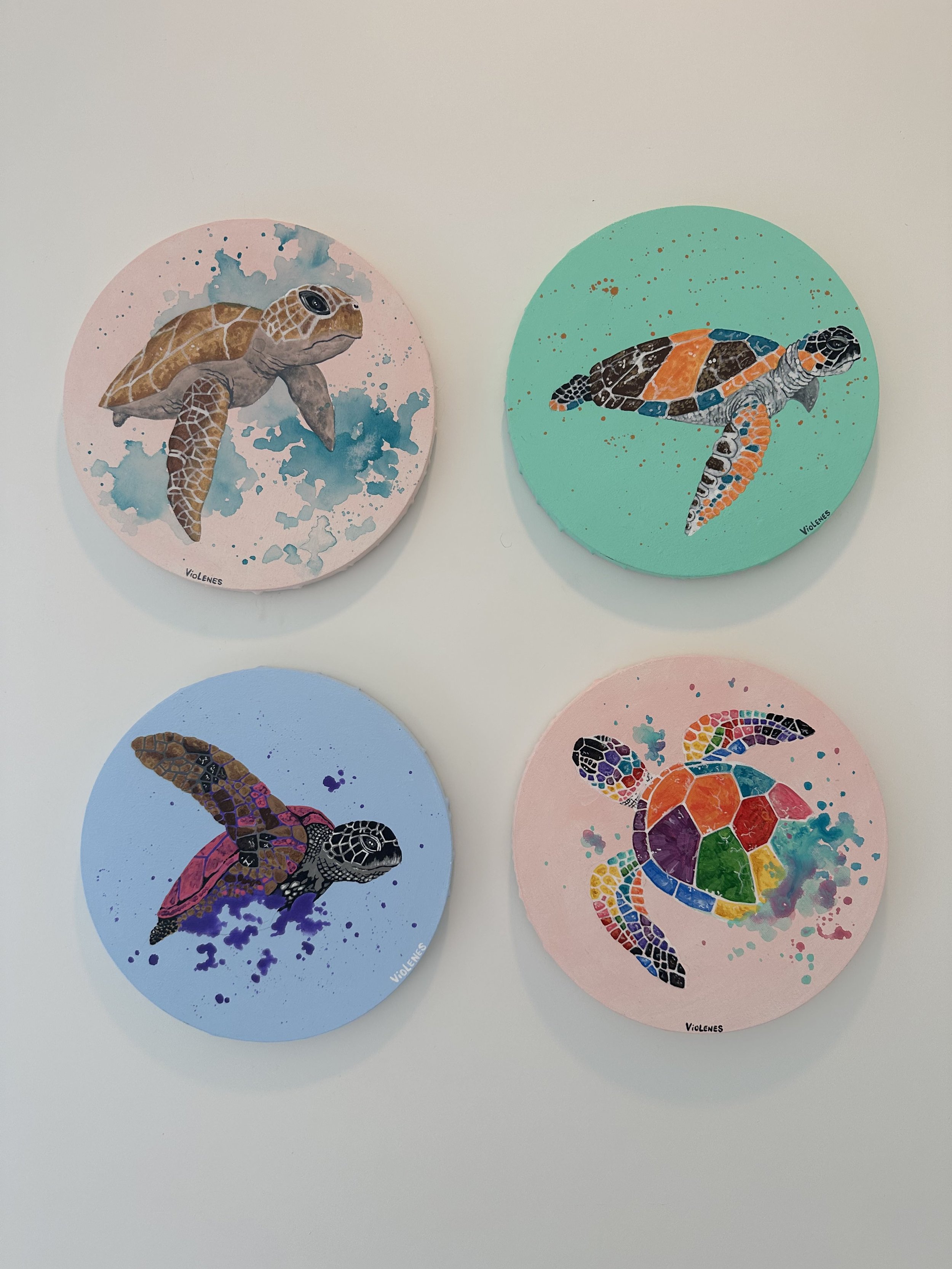 Four circular paintings of sea turtles in different colors and styles, hung on a white wall.