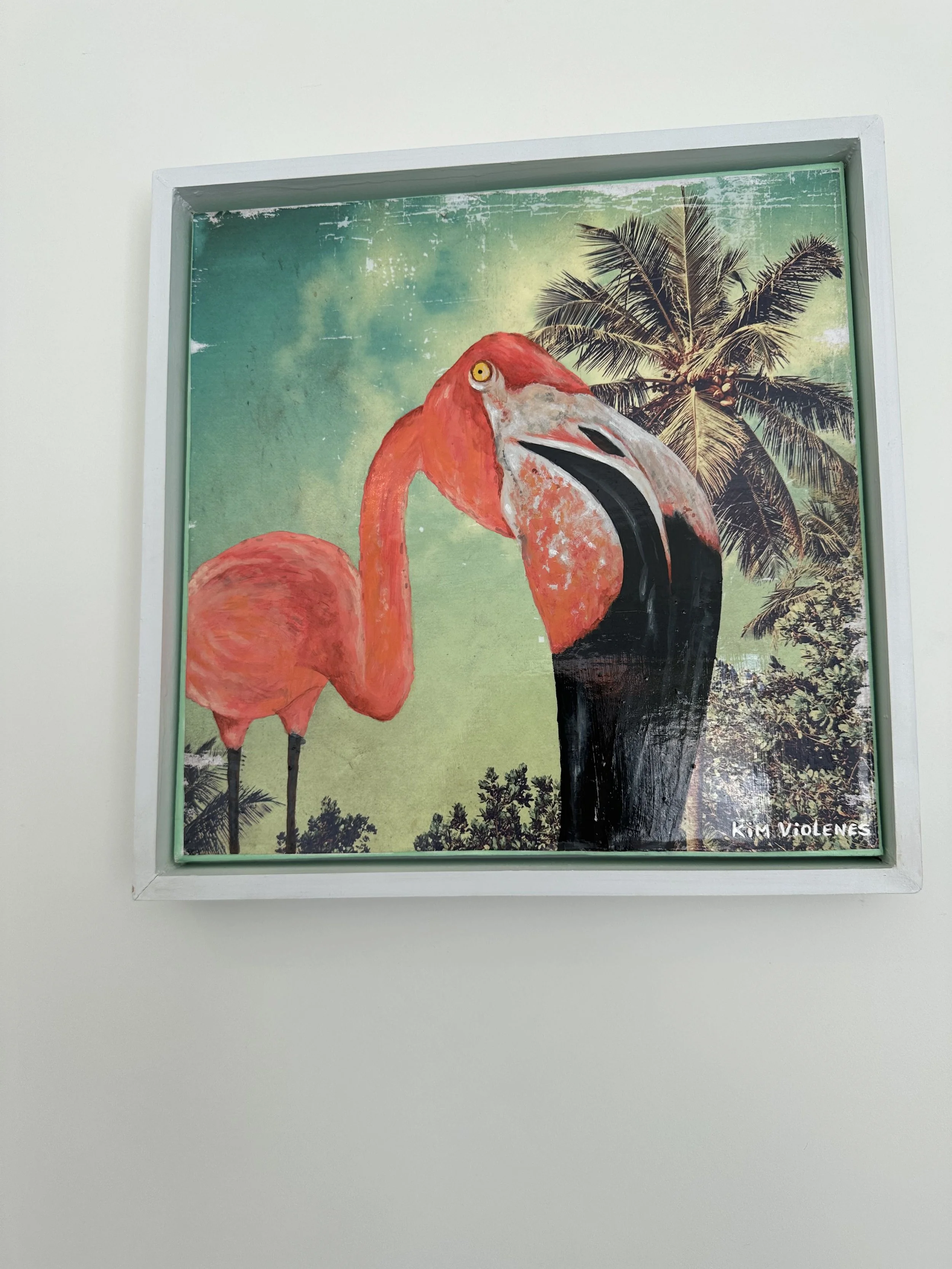 Painted artwork of two flamingos, one pink and one black, with a background of green sky and palm trees, signed Kim Violens.