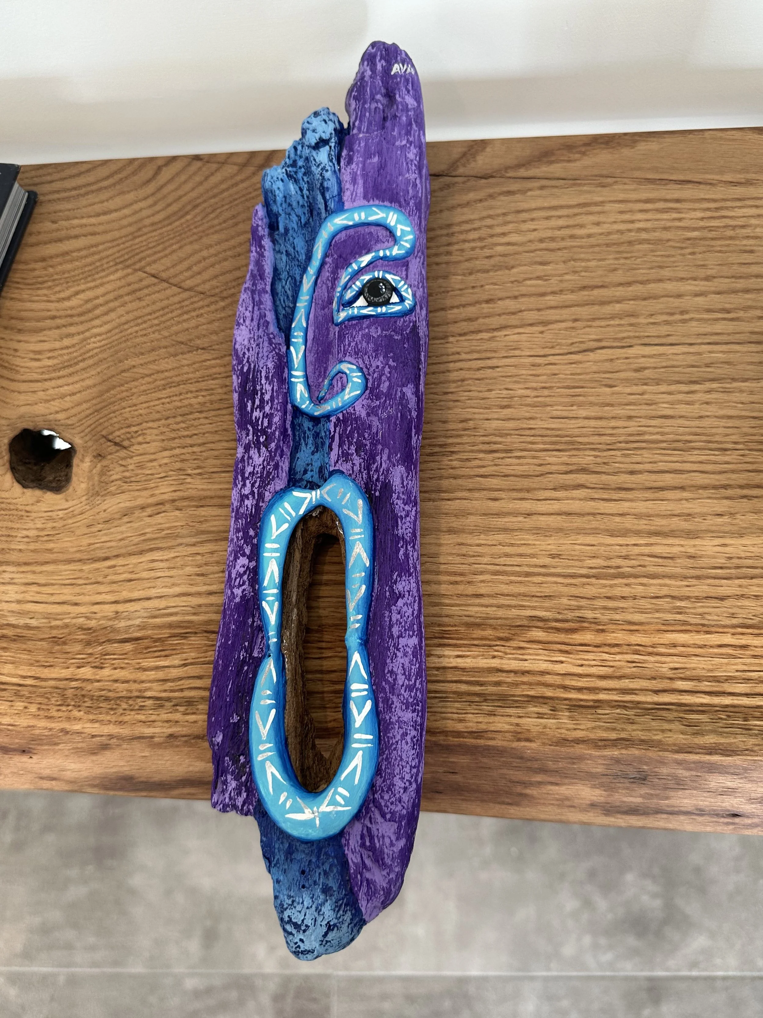 Decorative wooden plaque painted purple and blue with an embedded stylized eye and snake design.