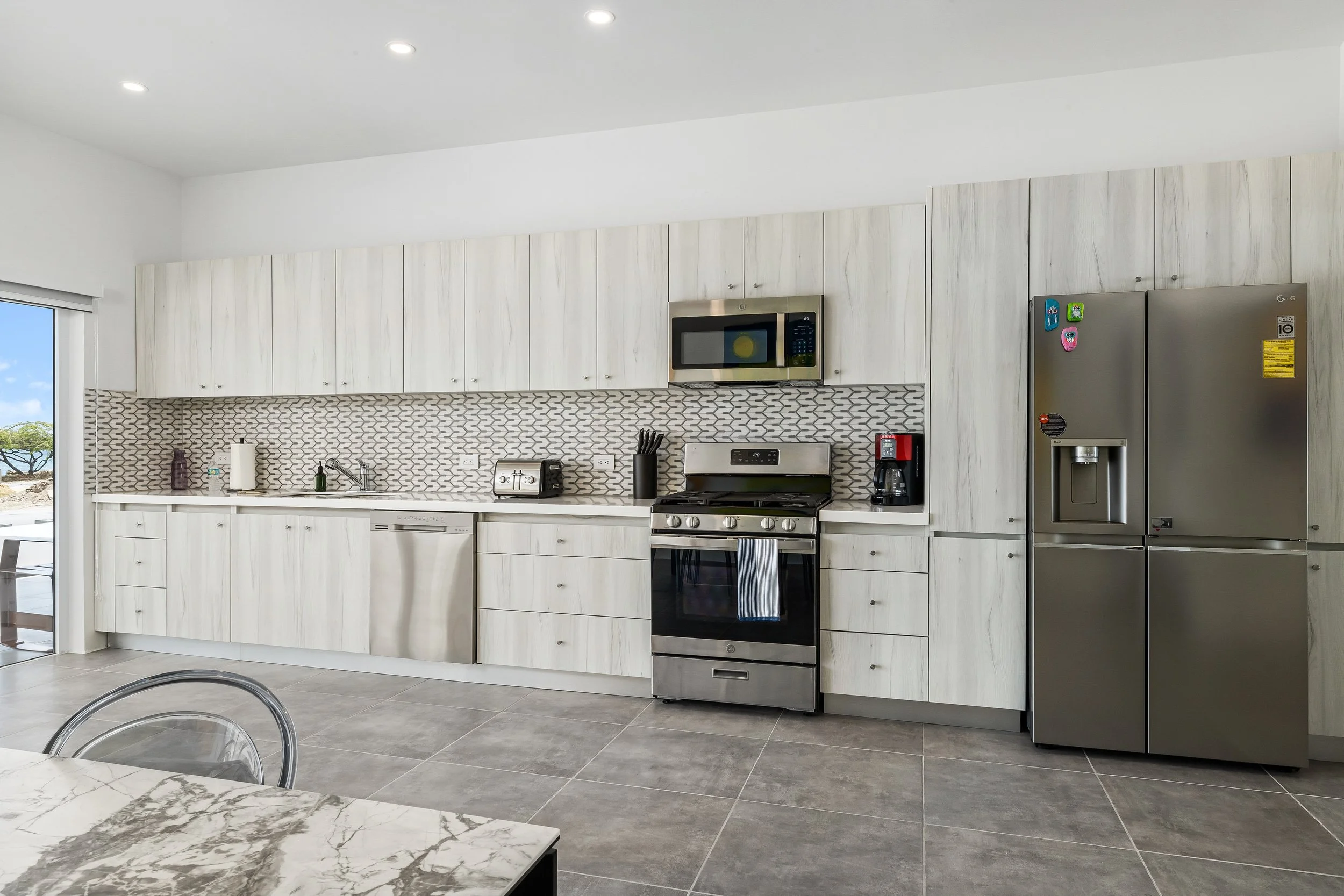 Modern kitchen with white cabinets, stainless steel appliances, a gray patterned backsplash, and a marble countertop.