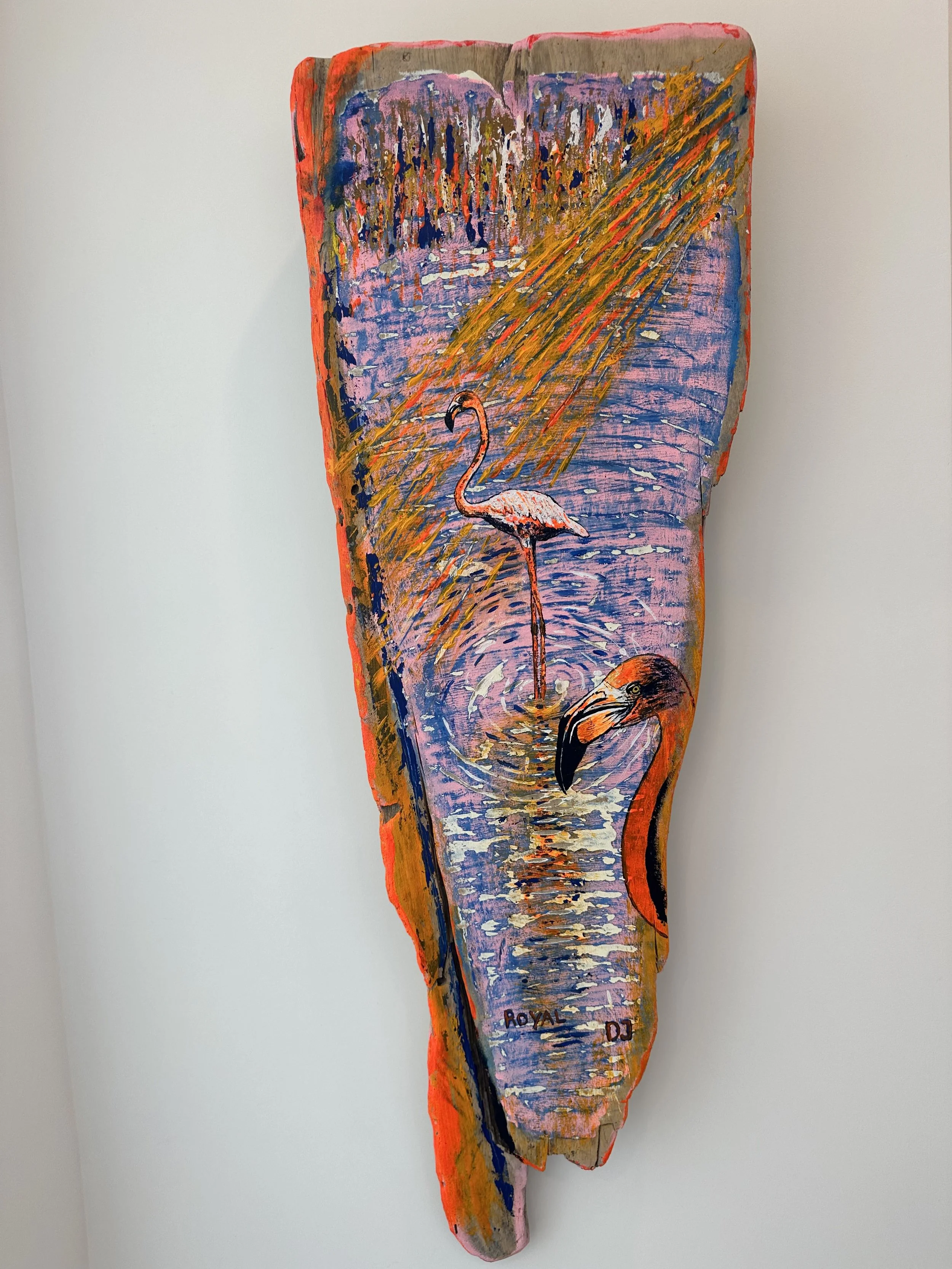 A colorful painted wooden plank features a flamingo standing in water, surrounded by abstract foliage and reflections, with the artist's signature "ROYAL DJ" at the bottom.