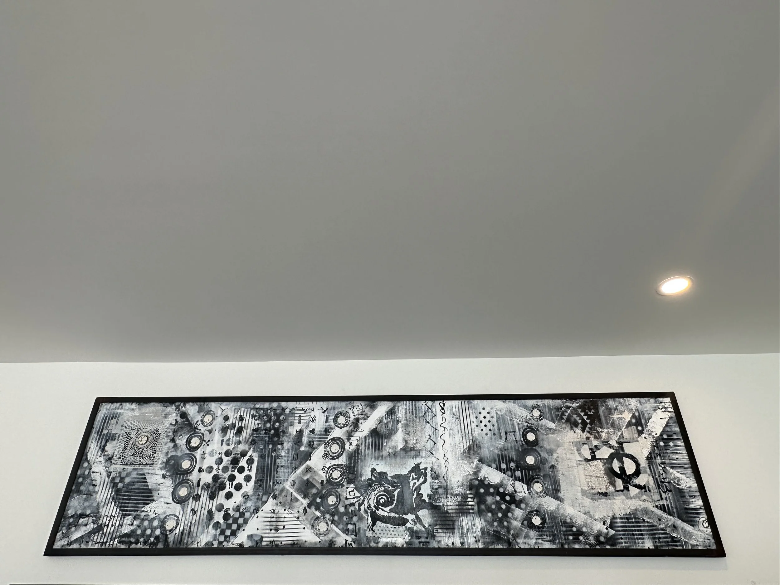 Black and white abstract artwork hanging on a white wall below a gray ceiling with a recessed light.