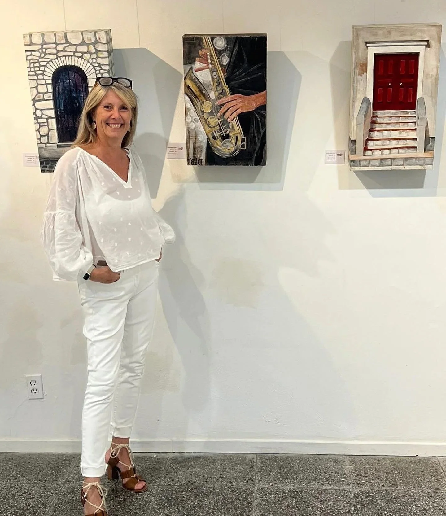 Woman in white standing next to artwork at an art gallery.
