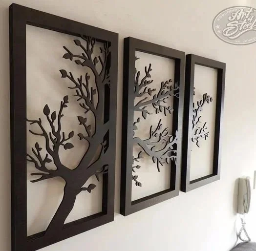 Decorative wall art with three black frames containing metal tree silhouettes mounted on a white wall.