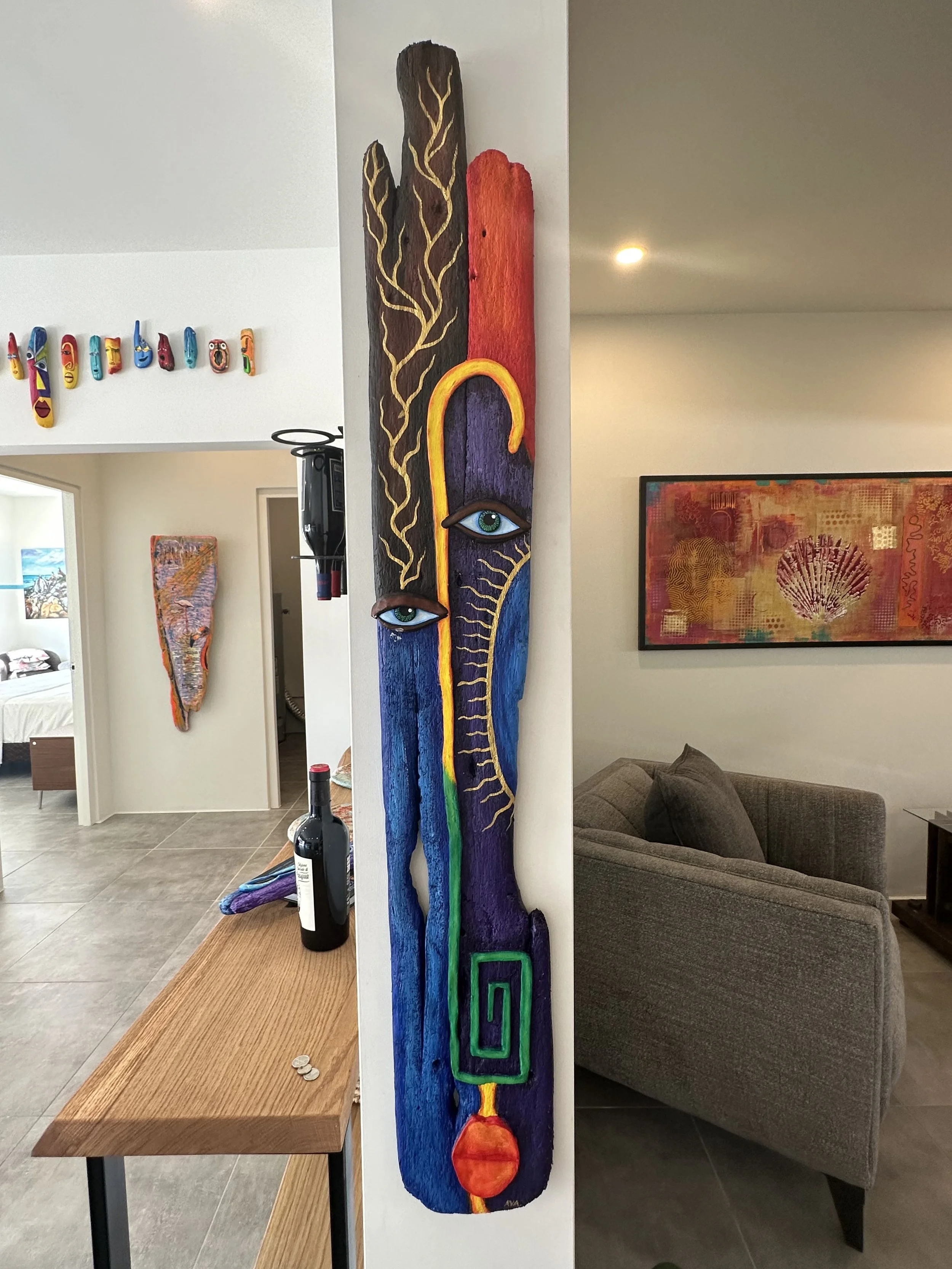 Colorful abstract wooden sculpture with eyes, featuring various shapes and patterns, mounted on a wall in a living room.