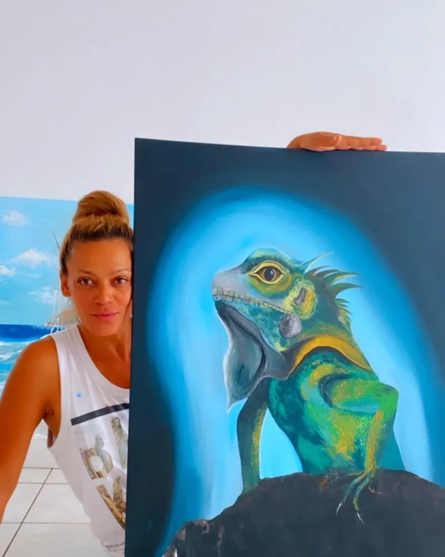 Woman holding a painting of a fantasy creature with a lizard body and a dinosaur skull face, standing on a rock.