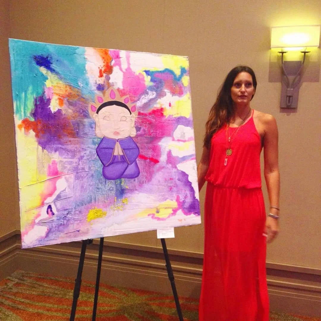 Woman in a red dress standing next to colorful abstract artwork on display in an indoor gallery.