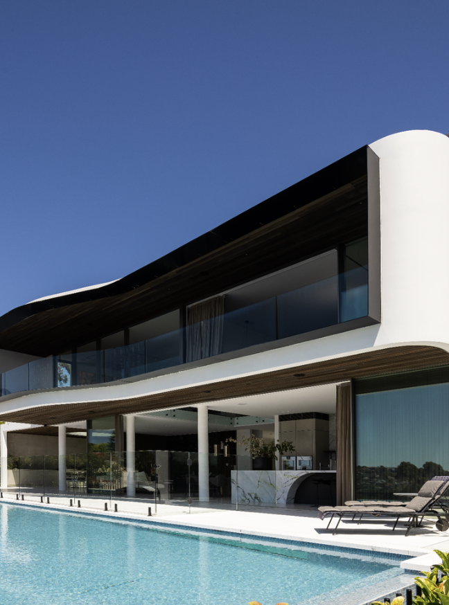 Modern house with large glass windows, curved white walls, and an outdoor pool under a clear blue sky.